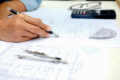 Cropped hand of engineer drawing on blueprint at office
