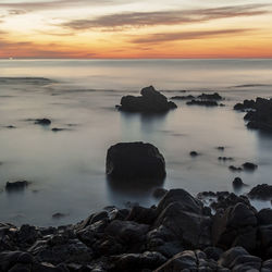 Rocks at sea shore against sky during sunset