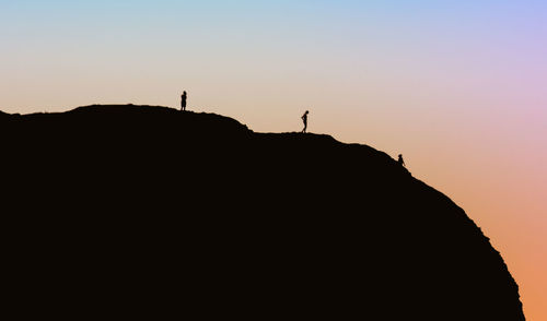 Silhouette people standing on rock against sky during sunset