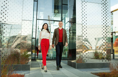 Respectable businessman and fashionable asian business woman walking near office. full length 