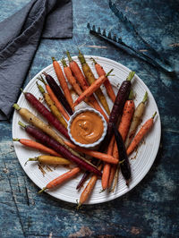 Roasted rainbow carrots on a round plate with sriracha mayo dip in the middle.