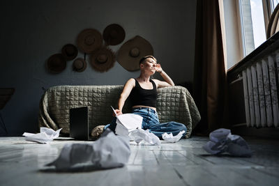 Woman professional content writer working with papers and laptop computer at home while sitting on