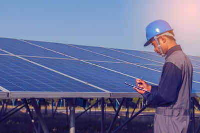 Male engineer examining solar panel against sky