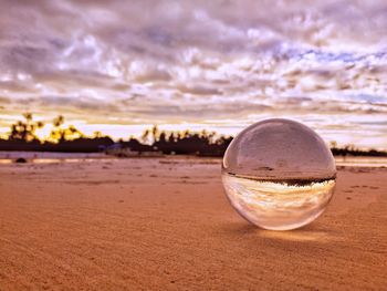 Close-up of crystal ball on beach against sky during sunset