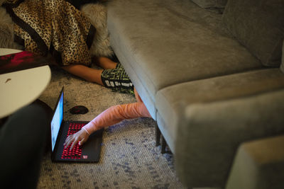 A 12-year old boy hides under couch while using a laptop computer
