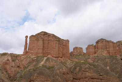 Low angle view of rocks on mountain against cloudy sky