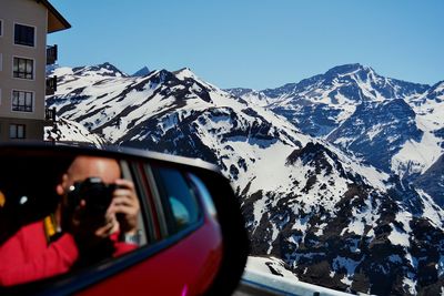 Reflection of man on side-view mirror of car against snowcapped mountain