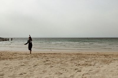 Woman running at beach against clear sky