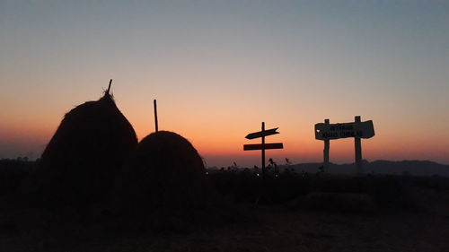 Silhouette cross on rock against sky during sunset