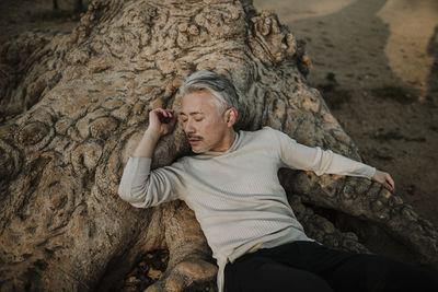 Mature man resting on tree roots in garden