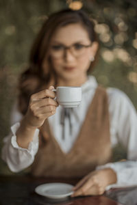 Portrait of young woman holding coffee cup while sitting in cafe