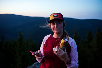 Portrait of man holding smart phone while standing on mountain