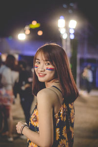 Portrait of smiling young woman standing outdoors at night