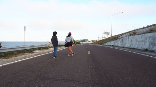 Rear view of people walking on road against sea