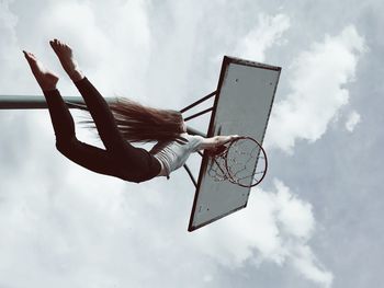 Low angle view of woman hanging on basketball hoop against sky