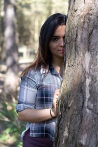 Portrait of young woman standing against tree trunk