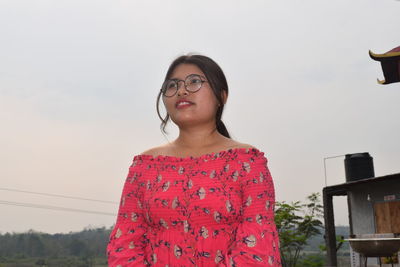 Portrait of young woman looking away against sky