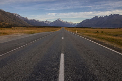 Empty road amidst field against sky