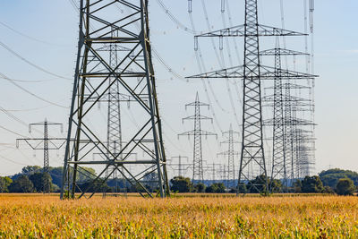 Low angle view of many electricity pylons with power lines against sky