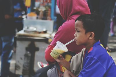 Side view of boy drinking drink while sitting outdoors