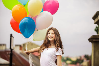 Portrait of smiling teenage girl holding balloons outdoors