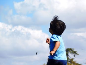 Side view of boy standing against sky