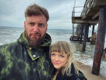 Portrait of father with daughter standing at beach against cloudy sky