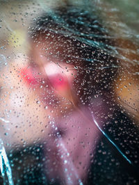 Close-up of woman seen through wet glass window