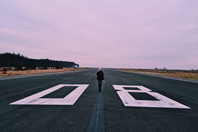 Man walking on airport runway against sky at sunset