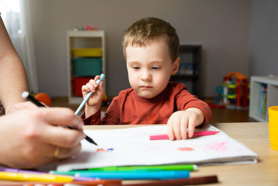 A cute little toddler boy of two years old with dad draws with markers in the album