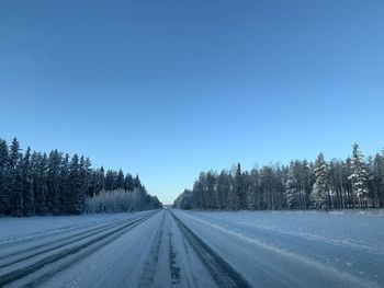 Road amidst trees against clear blue sky during winter