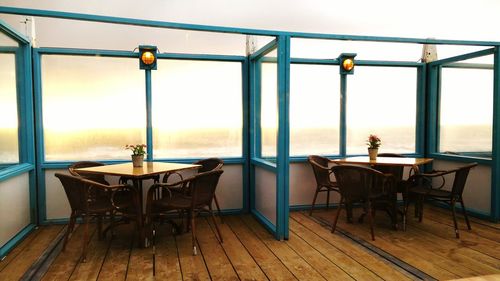 Empty chairs and tables arranged at cafe against sea during sunset