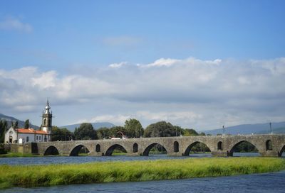 Arch bridge over river amidst buildings against sky