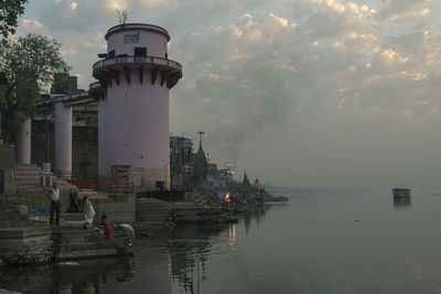 Lighthouse by sea against buildings in city