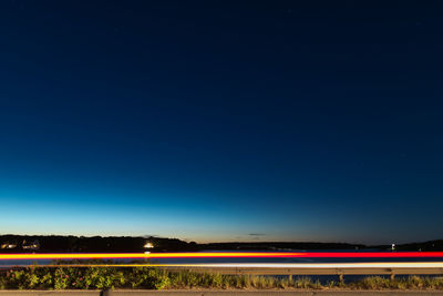 Light trails on field against clear blue sky at night