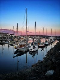 Sailboats moored in harbor at sunset