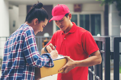 Female customer signing receipt while receiving package from delivery man at gate