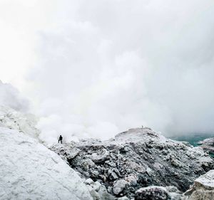 Distant view of man standing on rocky mountain against smoke