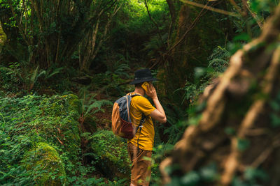 Caucasian man with a black hat and a backpack talking on the phone in the middle of the jungle