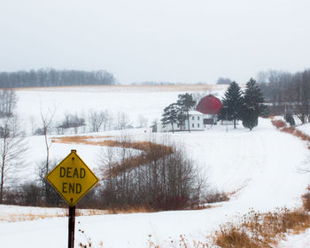 Road sign on snow field against sky during winter