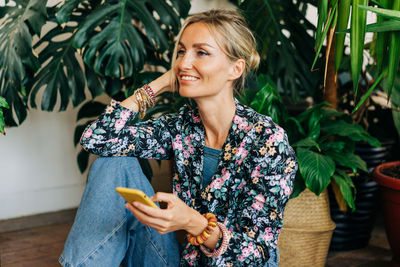 Young happy smiling woman sitting on the floor holding a mobile phone.