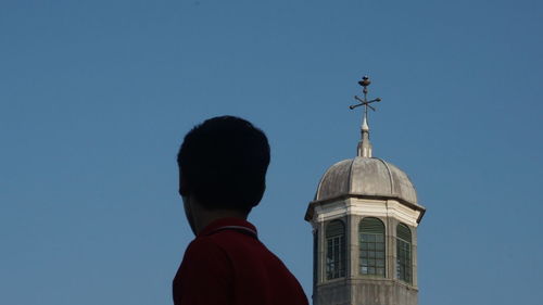 Low angle view of man against building against clear blue sky