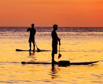 Silhouette people on sea against sky during sunset