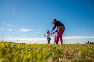 Mother holding hands of daughter while standing on land against sky