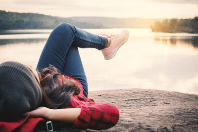Young woman lying on rock by lake against clear sky