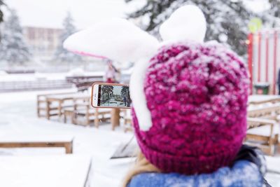 Rear view of woman wearing knit hat photographing snow in city