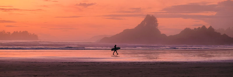 Silhouette woman walking at beach against sky during sunset