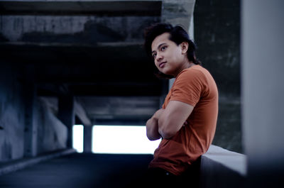 Side view of young man with arms crossed standing by railing