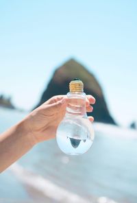 Close-up of hand holding bottle against water