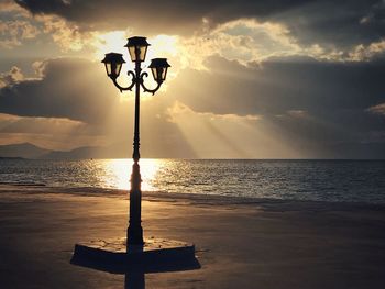 Street light by sea against sky during sunset